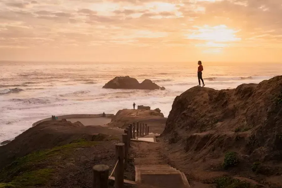 Due persone stanno sulle rocce che si affacciano sull'oceano ai Sutro Baths di 威尼斯人官网平台app.