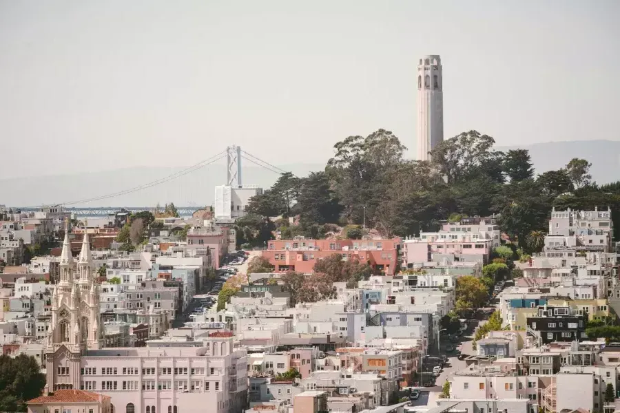 威尼斯人官网平台app的科伊特塔(Coit Tower)以海湾大桥(Bay Bridge)为背景，前景是一座覆盖着房屋的小山。.